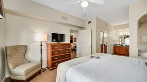 Une chambre d’hôtel avec un grand lit, une chaise, une commode, un téléviseur et un ventilateur de plafond.