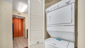 Une buanderie avec des machines à laver et des sèche-linge superposés, une porte et un sol carrelé.