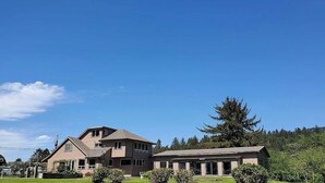 A two-story house with a large front lawn and a prominent tree. - Exclusive Cottage & Coastal Farmhouse Private Indoor Heated Pool ocean views. (Smith River)
