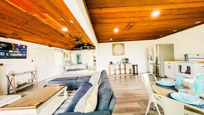 A spacious living area with a wooden ceiling, a sofa, a dining table, and a kitchen with a refrigerator and stove. - Exclusive Cottage & Coastal Farmhouse Private Indoor Heated Pool ocean views. (Smith River)
