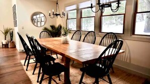 A dining room with a wooden table and black chairs, large windows with views of trees, and a chandelier.