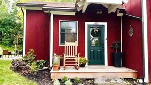 A red building with a porch, a green door, and a small garden area.