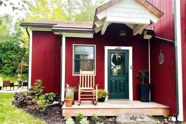A red building with a porch, a green door, and a small garden area.