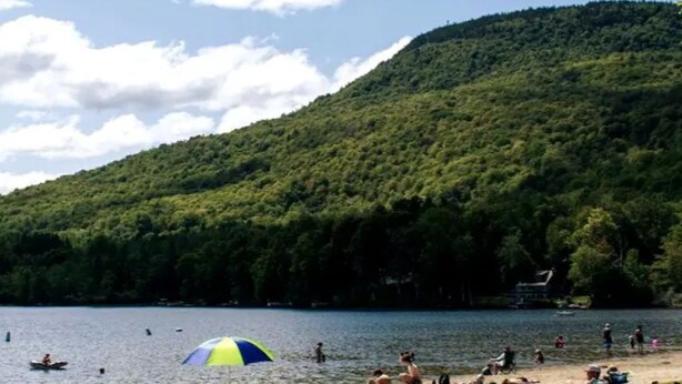 A lakeside scene with people relaxing on the beach and a few boats on the water.