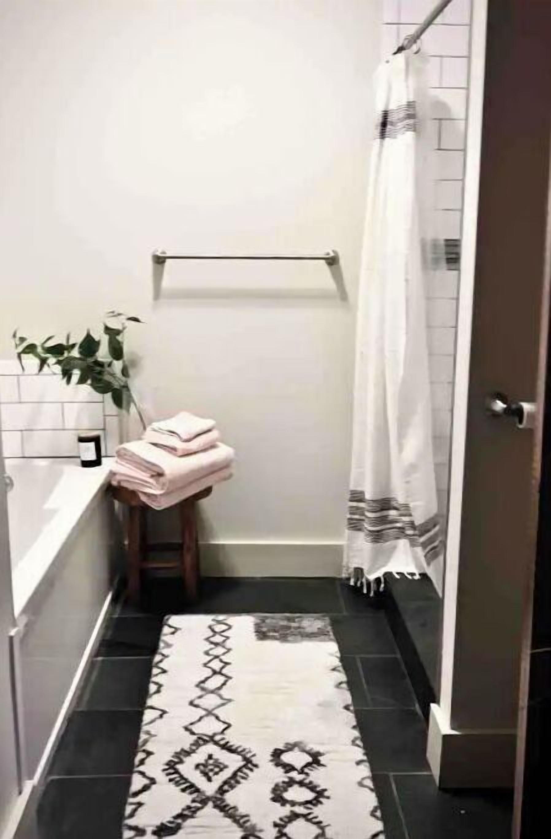 Een badkamer met een zwart-wit tapijt met patroon, een handdoekrek met opgevouwen handdoeken, een potplant en een douchegordijn.