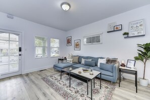 Una sala moderna con un sofá modular, una mesa de centro y una alfombra. Hay cuadros enmarcados en las paredes y una planta en maceta sobre una mesita auxiliar.
