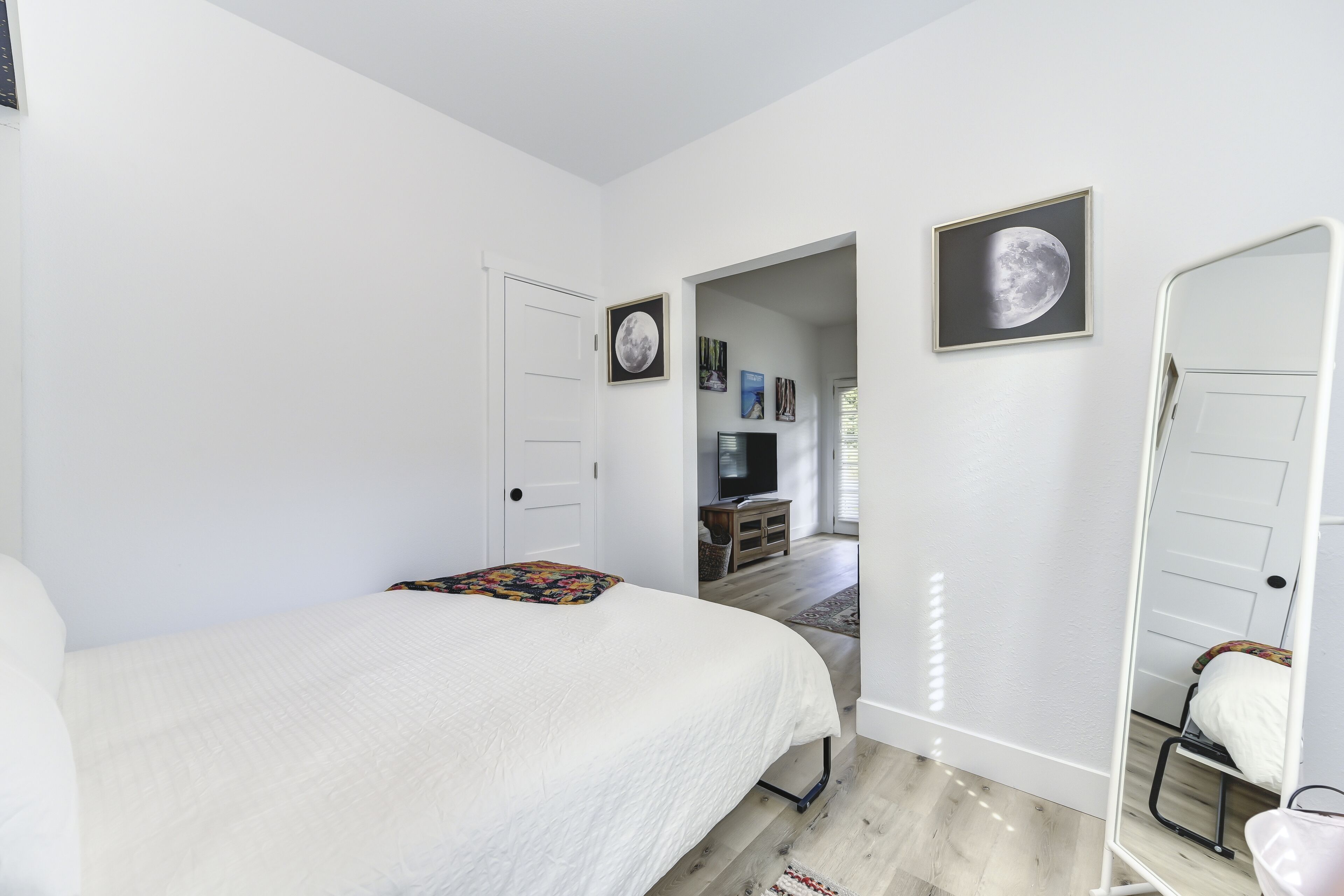 A bedroom with a bed, a chair, a door, and a hallway leading to another room.