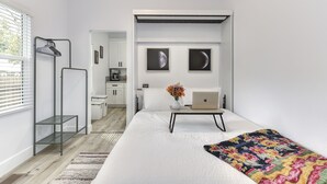 A modern bedroom with a bed, a desk with a laptop, a hanging light, and a view into the kitchen. - Modern Studio - North Oak Park/UC Med Center (Sacramento)