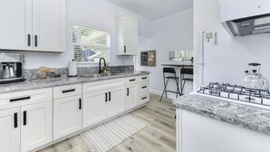 A modern kitchen with white cabinets, a granite countertop, a gas stove, and a window with blinds. - Modern Studio - North Oak Park/UC Med Center (Sacramento)