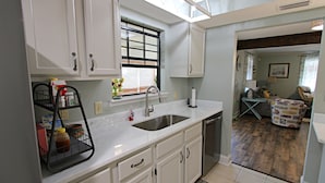 A kitchen with white cabinets, a stainless steel sink, and a window with blinds. - 🐋Come enjoy paradise with us and bring the family🐾🌊 (Foley)