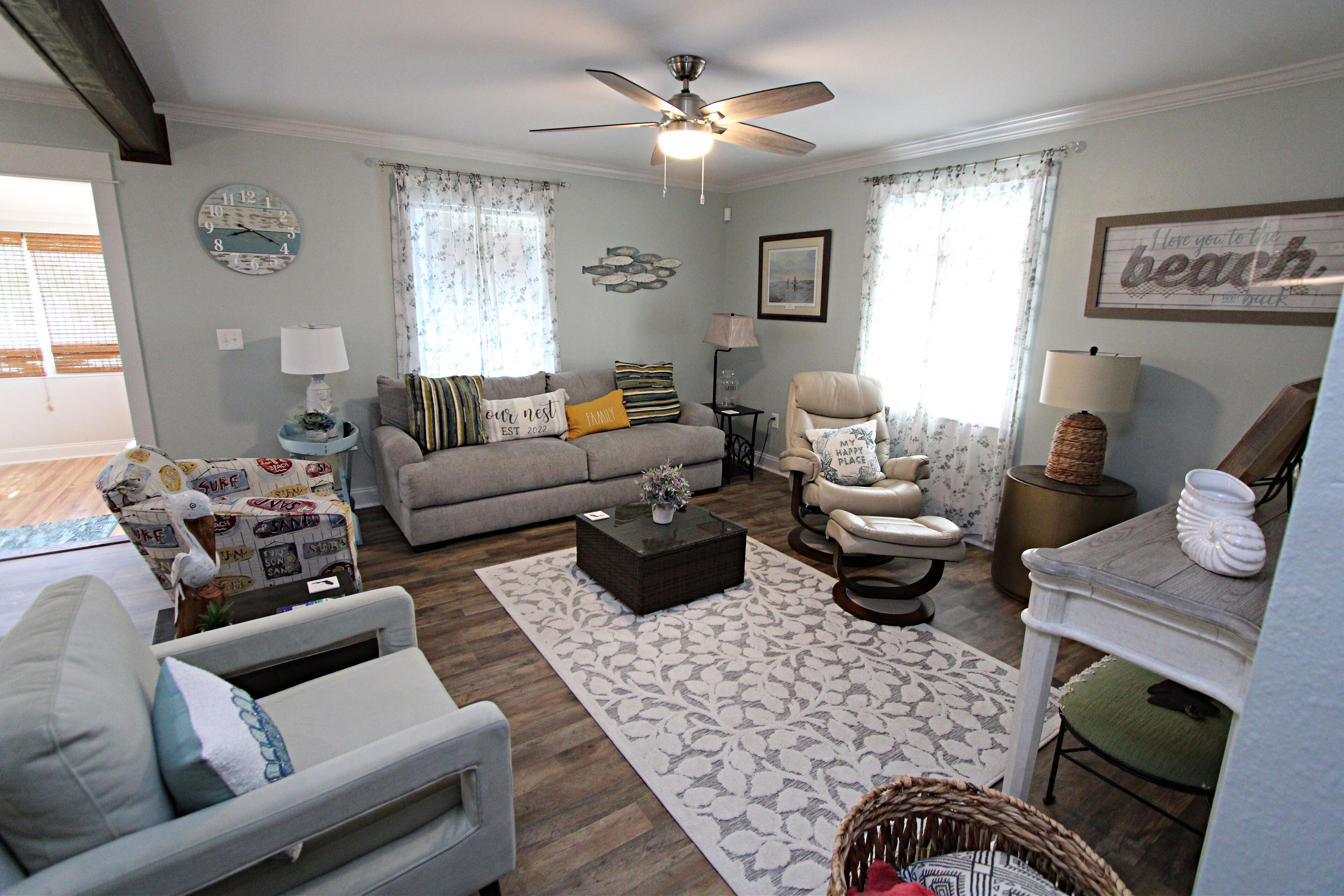 A living room with a sofa, armchairs, a coffee table, and a ceiling fan.