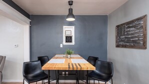 En matplats med ett träbord, fyra svarta stolar, en hängande lampa och två inramade skyltar på väggen.