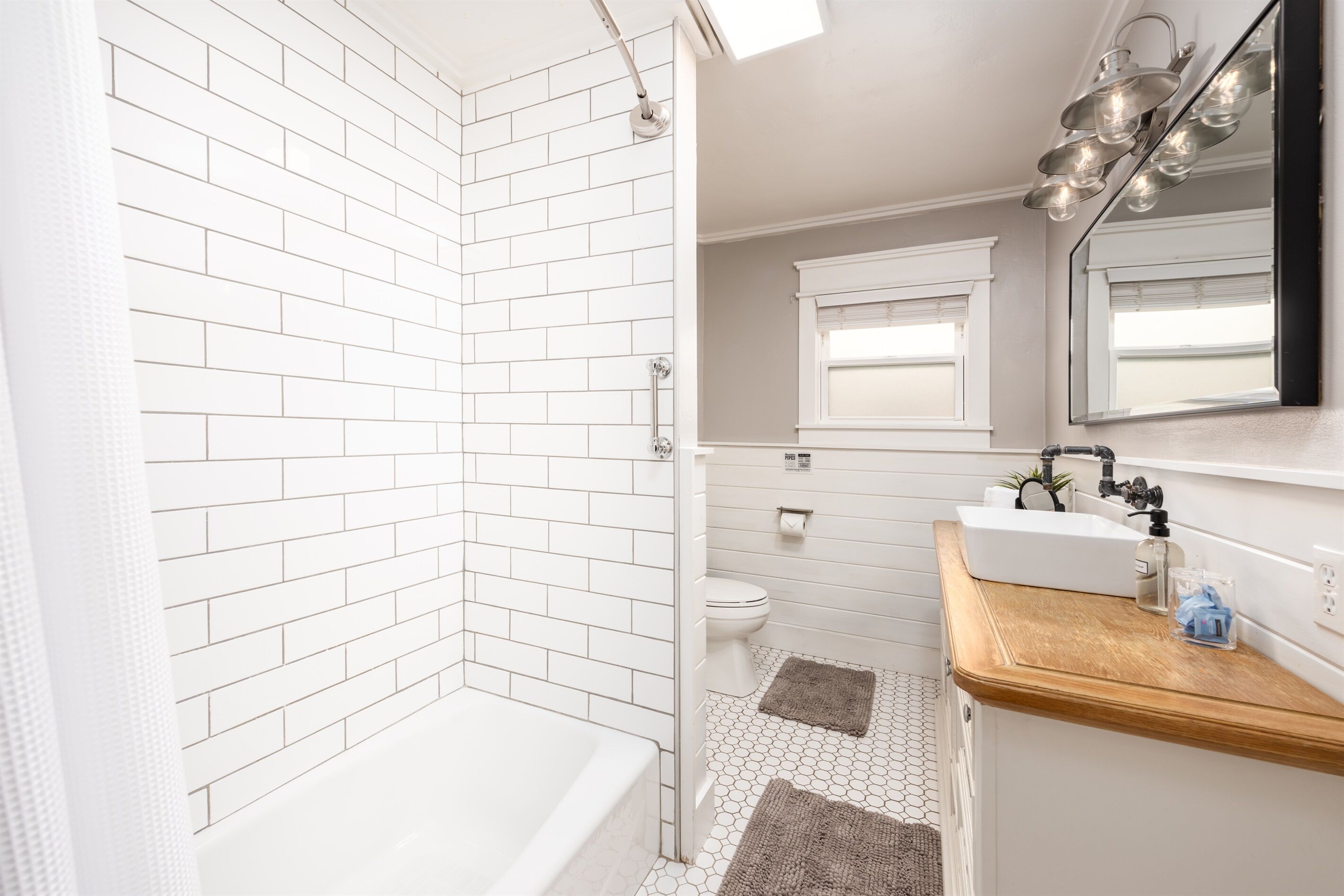 Une salle de bain moderne avec une douche carrelée de blanc, une baignoire, des toilettes et un lavabo doté d’un plan de travail en bois.