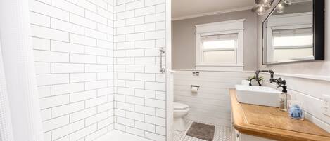 Une salle de bain moderne avec une douche carrelée de blanc, une baignoire, des toilettes et un lavabo doté d’un plan de travail en bois.