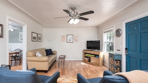 Un salon doté d’un ventilateur de plafond, d’un téléviseur, d’une porte bleue et d’un coin repas avec une table et des chaises.