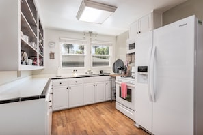 Una cocina con armarios blancos, un refrigerador blanco, una encimera de madera, una ventana y un reloj en la pared.