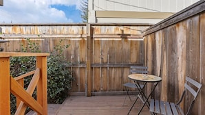 Une terrasse en bois avec une table et des chaises, une clôture en bois et un petit espace aménagé en jardin.