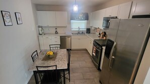 A compact kitchen with white cabinets, a stainless steel refrigerator, a microwave, and a sink. There is a dining table with chairs and a small plant on the table. - HOT TUB SUNFLOWER OASIS HOME (Sherman)