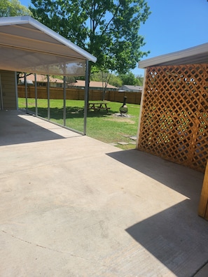 A covered patio area with a picnic table and a grill, surrounded by a wooden fence and trees. - HOT TUB SUNFLOWER OASIS HOME (Sherman)