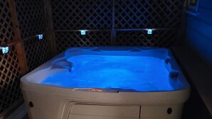 A hot tub with a built-in seat and steps, surrounded by a wooden fence and illuminated by small lights. - HOT TUB SUNFLOWER OASIS HOME (Sherman)