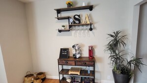 A corner of a room with a wooden floor, a wall-mounted shelf with decorative items, a potted plant, and a small wooden table with various objects. - HOT TUB SUNFLOWER OASIS HOME (Sherman)