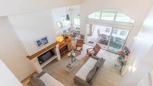Ein großzügiger Wohnbereich mit einer Couch, einem Couchtisch und einem Fernseher. Es gibt einen Balkon mit Sitzgelegenheit im Freien.