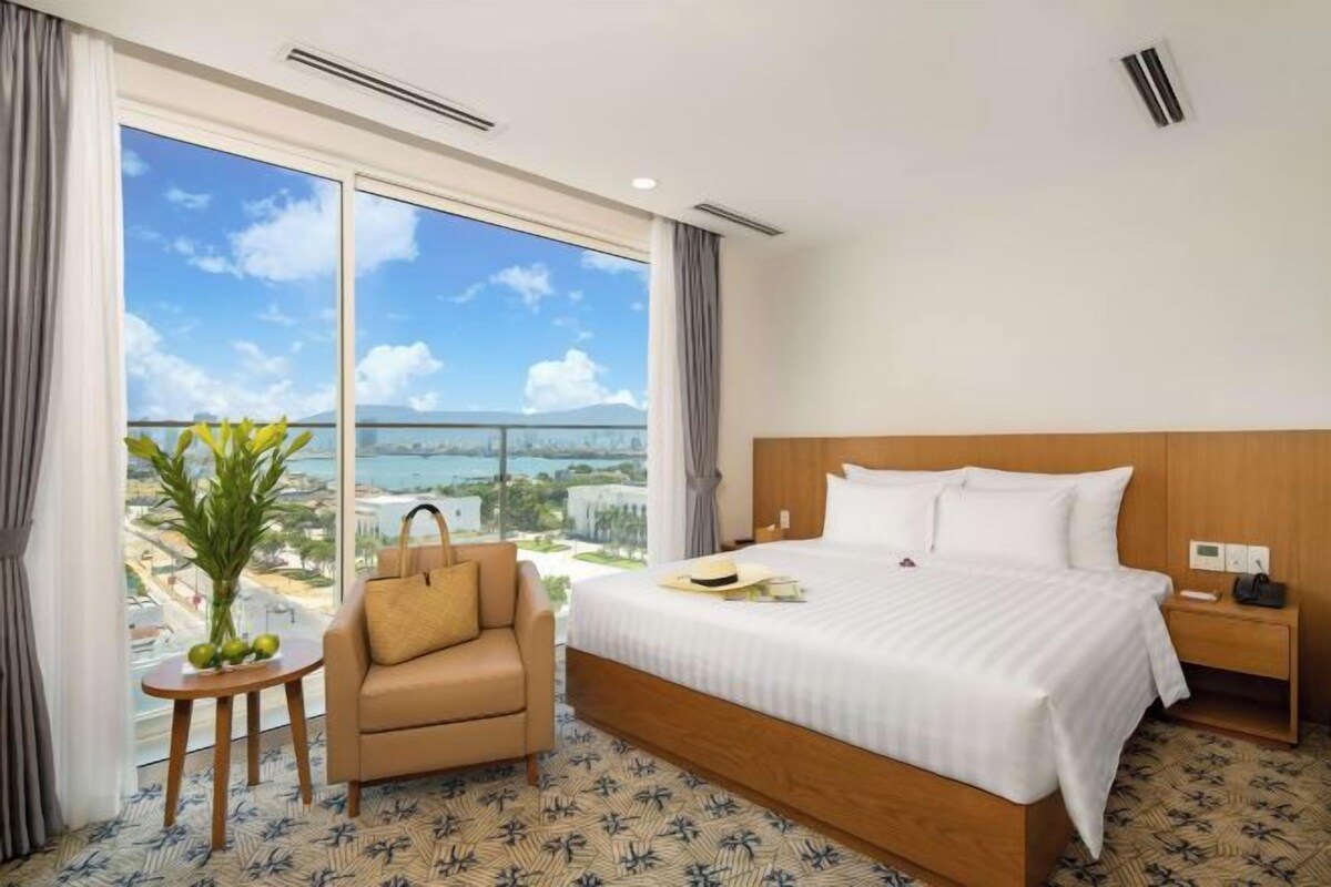 A hotel room with a large bed, a chair, a small table with a plant, and a nightstand.