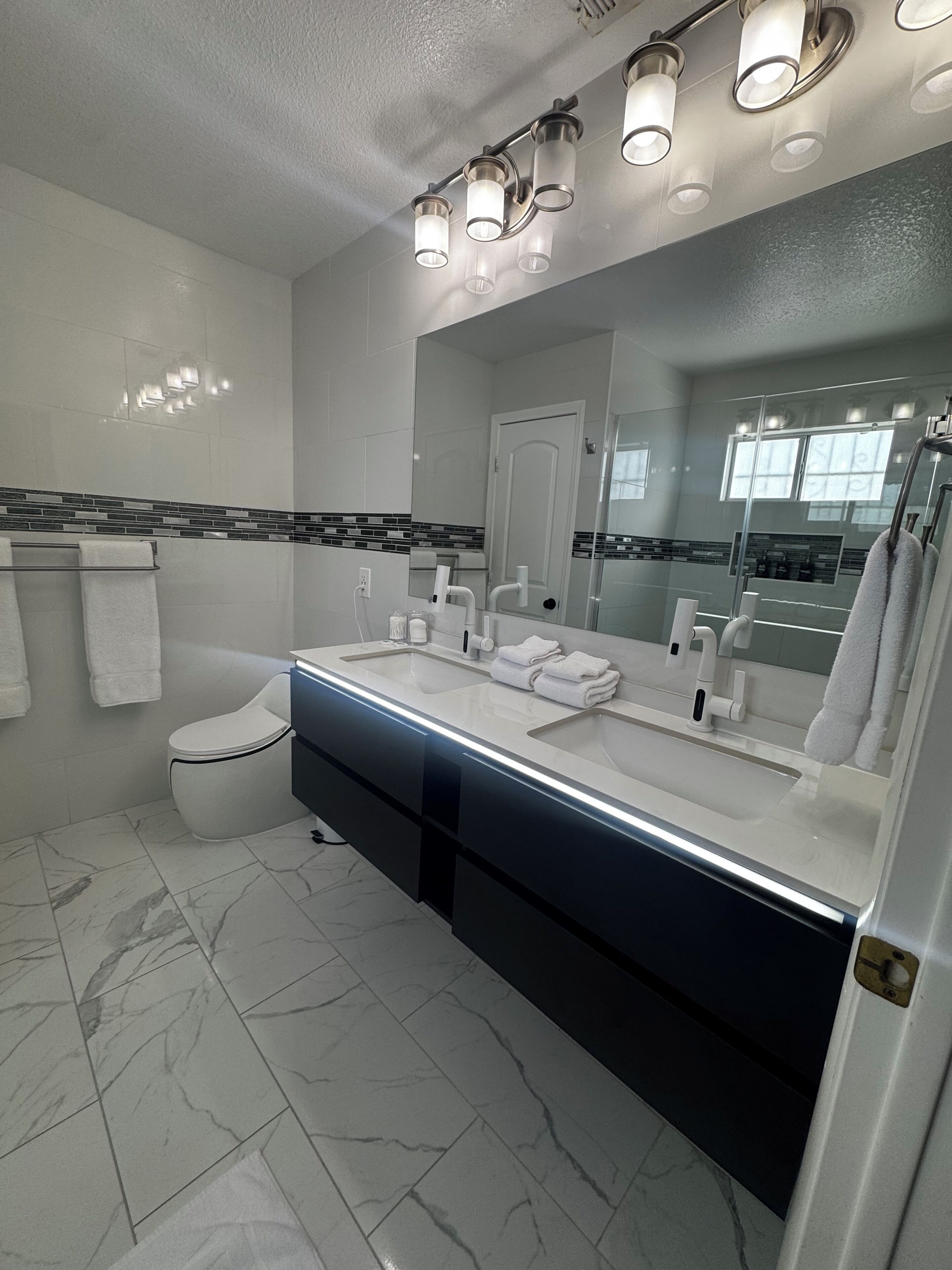 Un bagno moderno con uno specchio grande, una vasca, un water e un mobile lavabo.