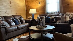 A cozy living room with a leather sofa, a round coffee table with decorative items, and a cowhide rug.
