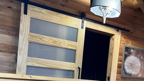 A wooden cabin interior with a balcony, a sliding door, and a ceiling light fixture.