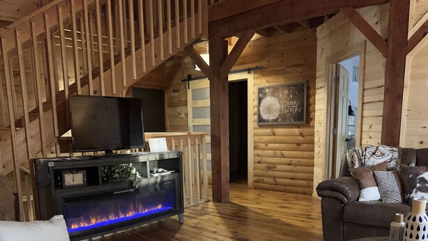 A cozy log cabin interior with a fireplace, wooden furniture, and a cowhide rug.
