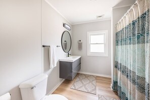 Ein modernes Badezimmer mit Toilette, Waschbecken, Spiegel und Duschvorhang.