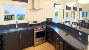 Una cucina moderna con un'isola grande, elettrodomestici in acciaio inossidabile, mobili scuri e vista sull'oceano.