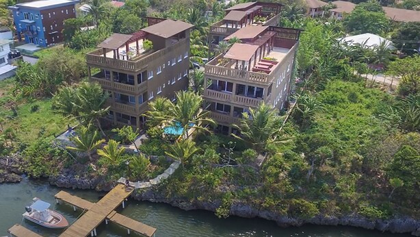 Un edificio a più piani con balconi, immerso nel verde e con un pontile e una barca.