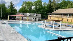 Ein Swimmingpool mit einem umzäunten Bereich, Liegestühlen und einem Gebäude mit einem Strohdach im Hintergrund.