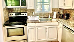 Eine Küche mit weißen Schränken, einem schwarzen Herd, einer Mikrowelle, einer Spüle und einem Fenster über der Spüle.
