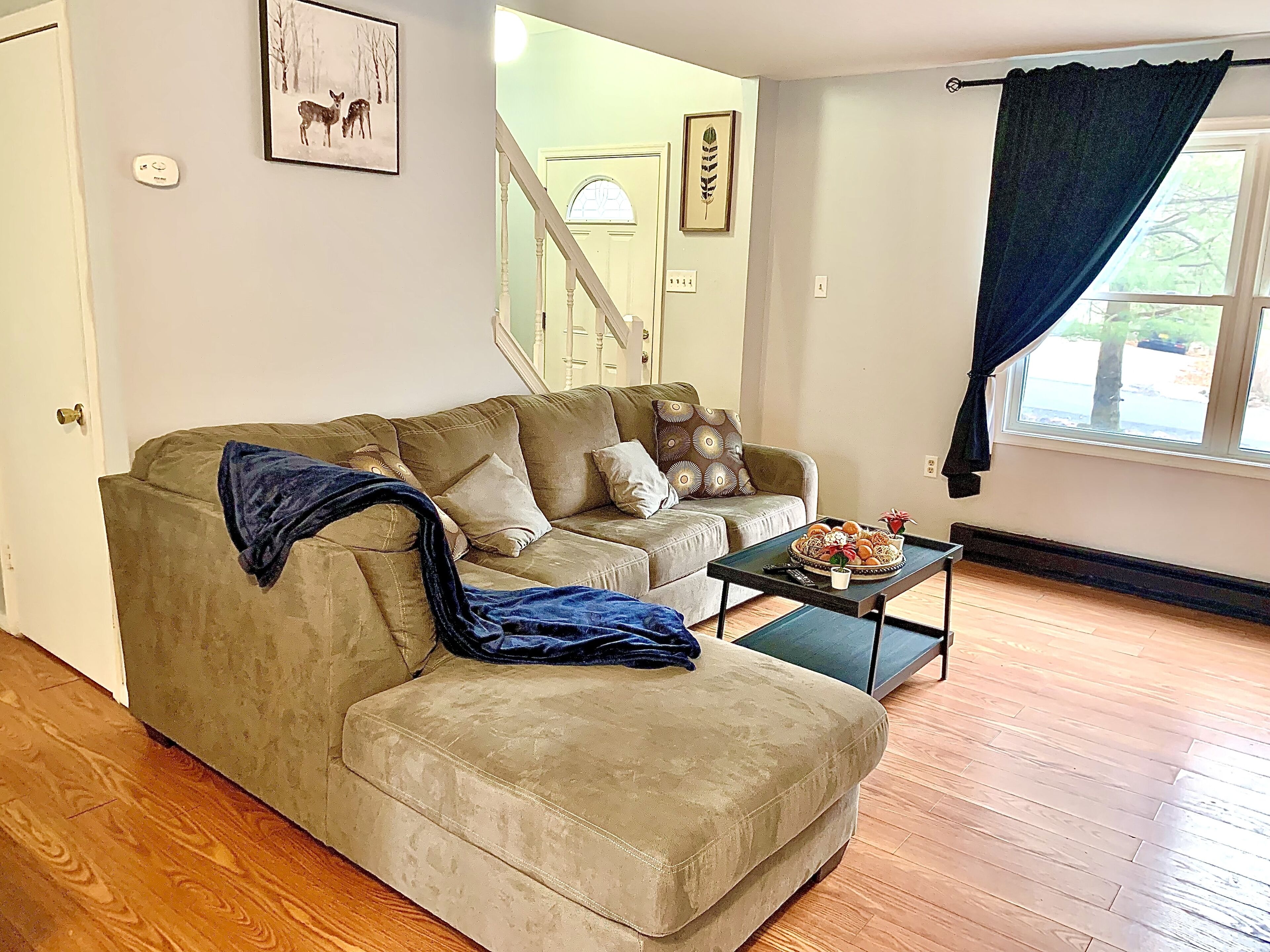 Un salon avec un canapé beige, une table basse et une fenêtre avec un rideau.