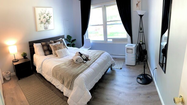 Une chambre à coucher bien rangée, avec un lit, une lampe de chevet et une fenêtre avec des rideaux.