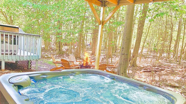 Ein Whirlpool inmitten von Bäumen mit einer Holzterrasse und Stühlen.