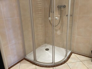Un vestuario de ducha con paredes de vidrio, suelo blanco, ducha y un mando.