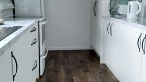 A compact kitchen with white cabinets, a microwave, a coffee maker, and a world map on the wall. - Modern unit 2 minute nature path to the lake (Manapouri)