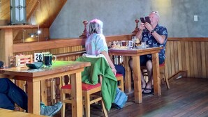 A rustic wooden interior with high ceilings and exposed beams, featuring wooden tables and benches, a lantern, and a window with a colorful frame. - Modern unit 2 minute nature path to the lake (Manapouri)