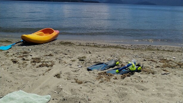 A kayak and diving gear on a sandy beach with a calm lake and mountains in the background. - Modern unit 2 minute nature path to the lake (Manapouri)