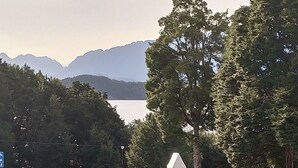A dining table with food and drinks, a person seated, and a scenic view of a lake and mountains. - Modern unit 2 minute nature path to the lake (Manapouri)