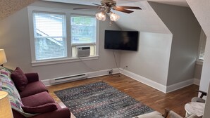 A room with a ceiling fan, a large window with blinds, a flat-screen TV mounted on the wall, a red couch, a patterned rug, and a marble table. - Bristol Short Stay for work, Nascar,Music, 1bdrm King size, Queen sleeper sofa.  (Bristol)