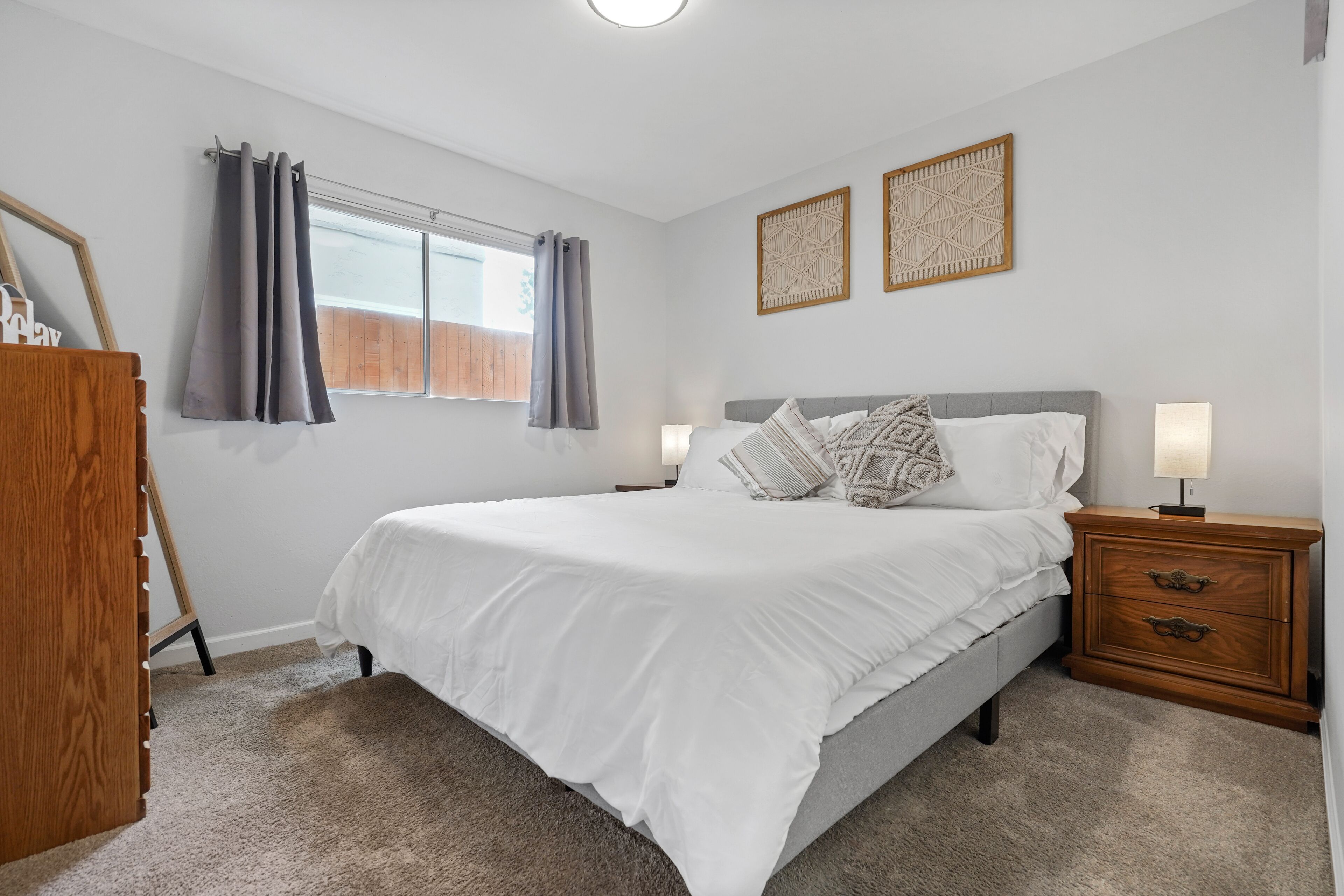 A bedroom with a bed, bedside tables, a dresser, and a window with curtains.