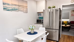 Una cocina moderna con un refrigerador de acero inoxidable, un microondas y una zona de comedor con una mesa y sillas blancas.