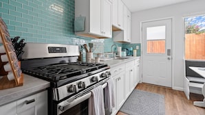 Una cocina moderna con armarios blancos, estufa negra y azulejos de salpicadero color turquesa.