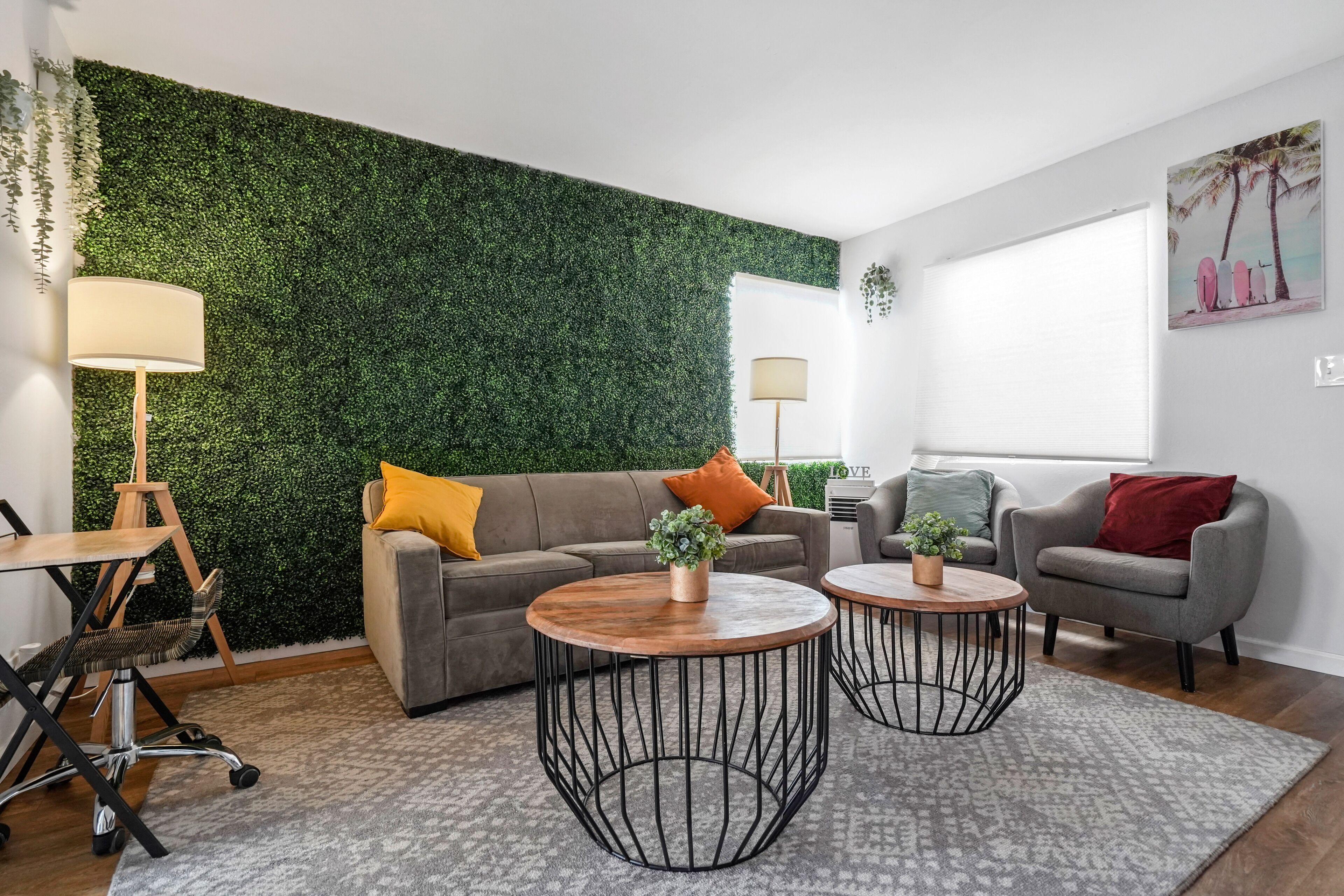 Un salon moderne avec un mur vert, deux tables basses rondes, un canapé gris et un fauteuil rouge.