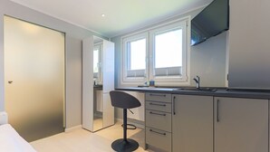 A modern kitchen with a bar stool, a large window, and a flat-screen TV mounted on the wall. - Palenque - Apartment Palenque (Sylt-Ost)